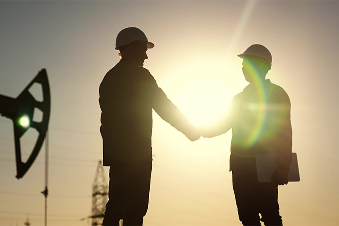 Workers in safety hats shaking hands outside at sunset